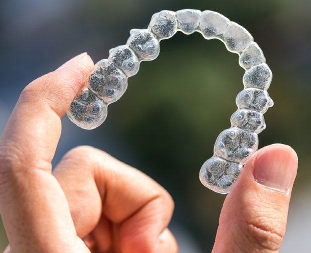 Example of Invisalign dentures held between a finger and thumb